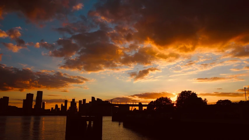 a sunset over a city with clouds, water and trees