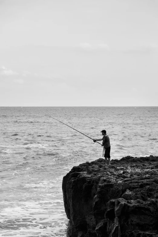 a man on the rocks with his fishing pole and boat