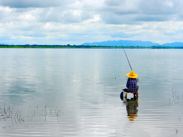 a man sitting on a rock fishing with a yellow hat