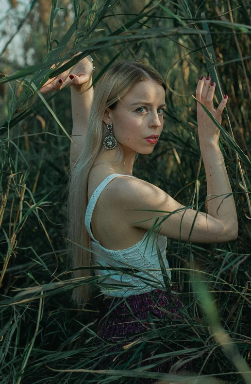 a woman stands amongst thick grass while holding her arm out