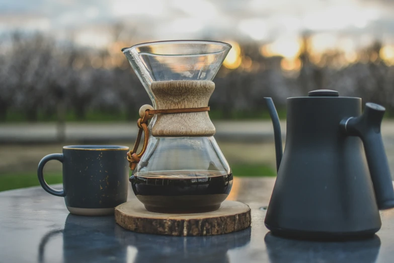 a coffee pot, glass carafe and two cups sitting on a table outdoors