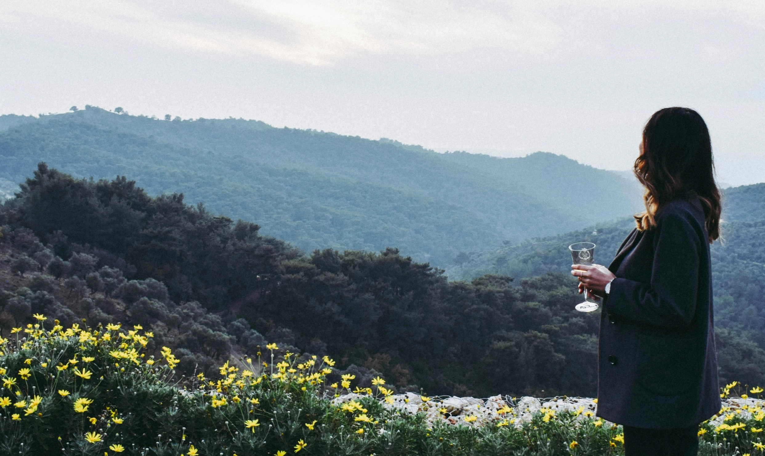 woman drinking water out of a wine glass standing in a flowered meadow