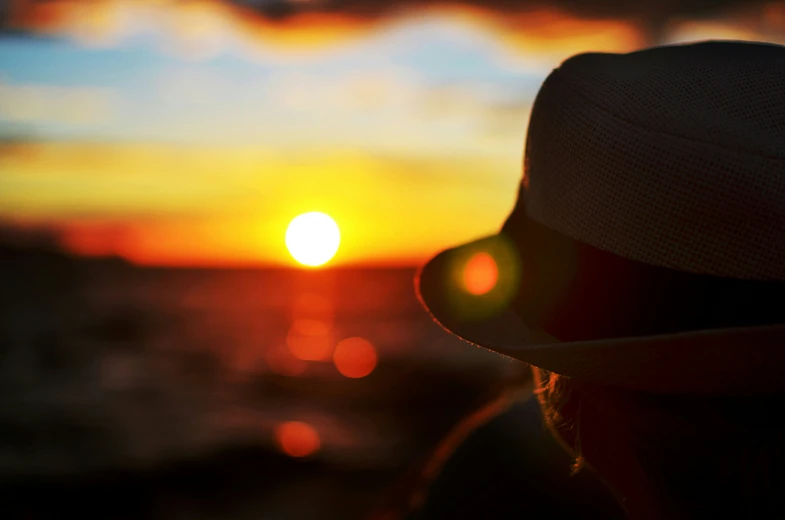 woman in white hat overlooking the sunset with water