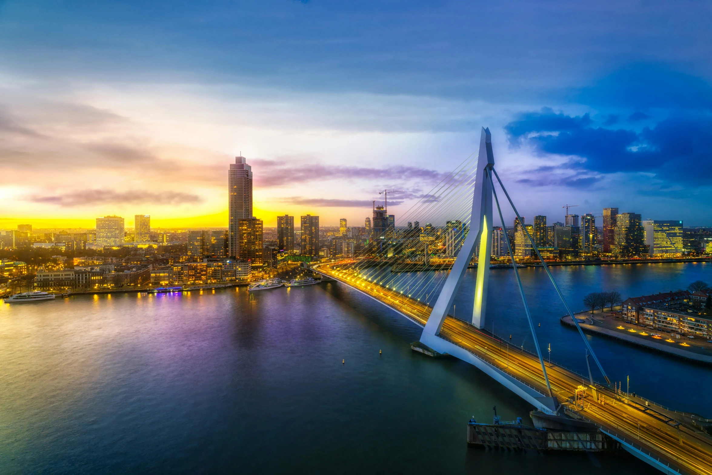 a city skyline is seen at dusk as the sun sets over the bridge