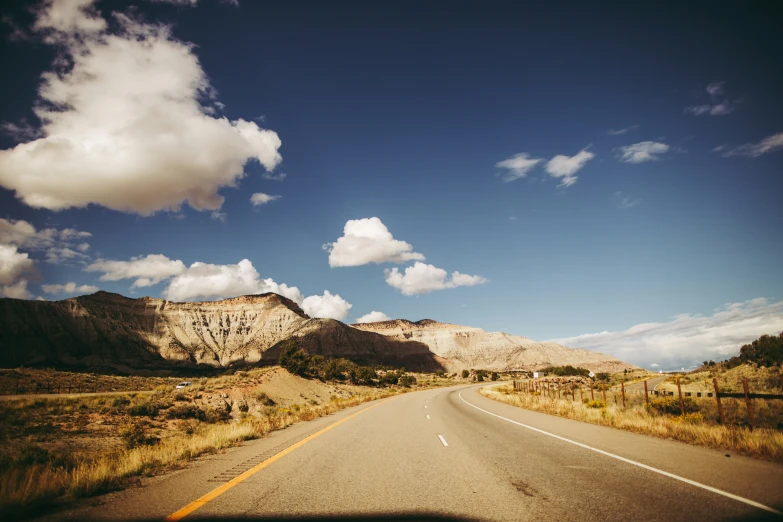 the clouds are above mountains as one goes by on the highway