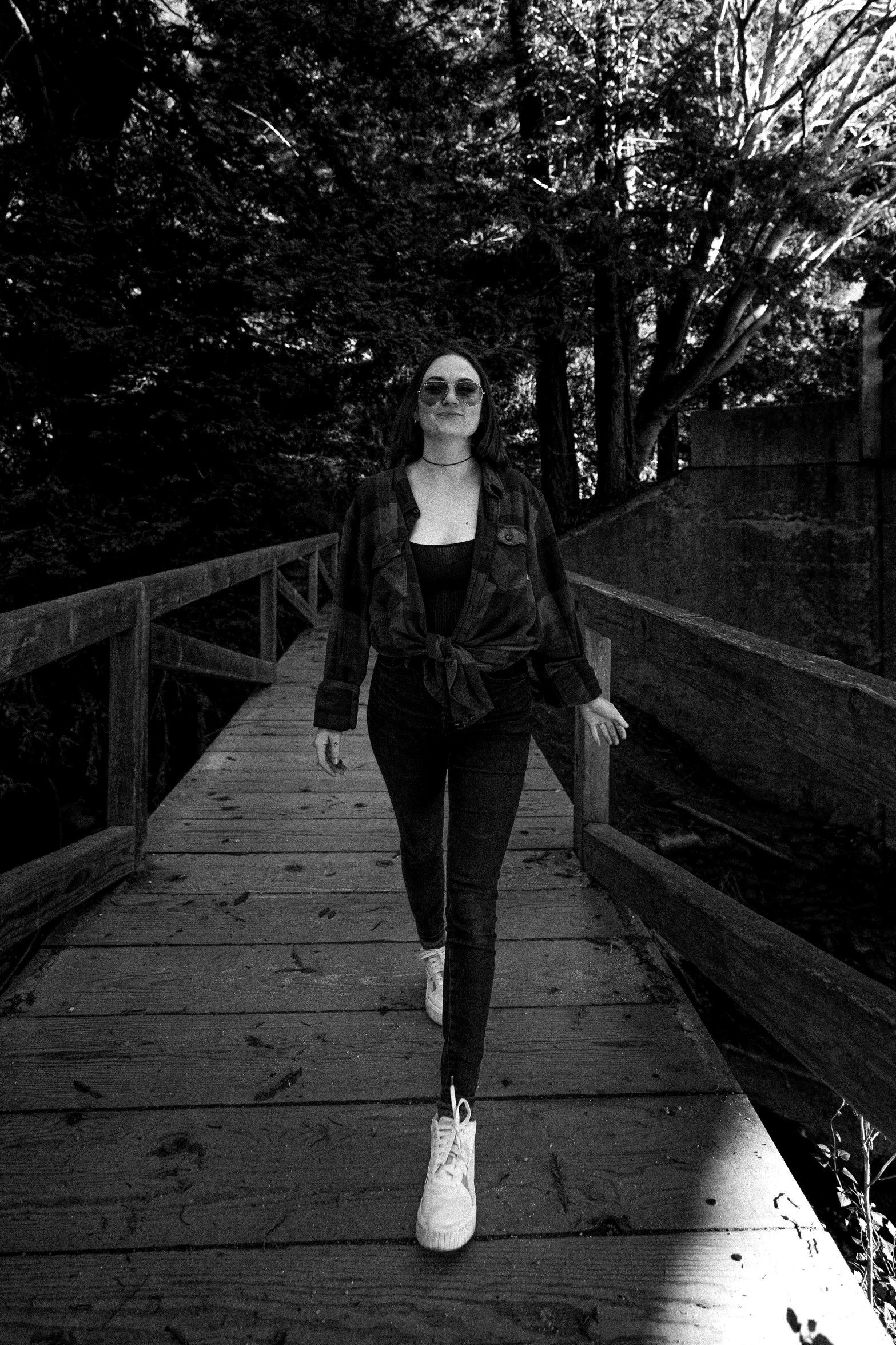 a woman in sunglasses walking across a bridge