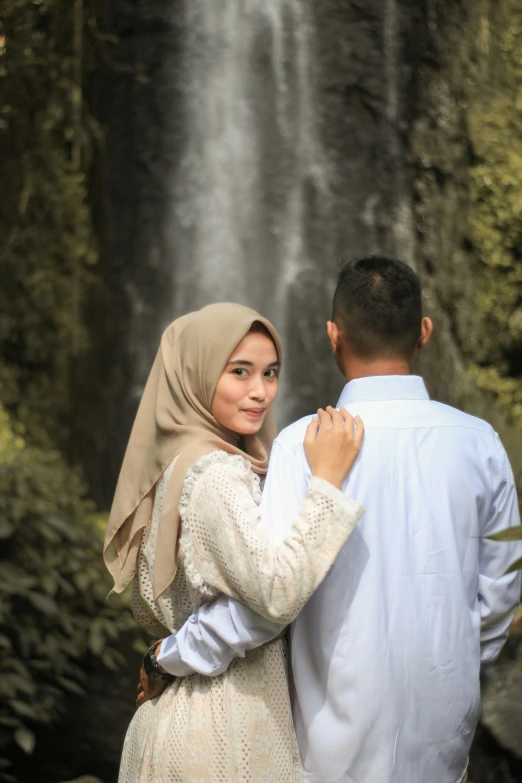 the man and woman are posing in front of a waterfall