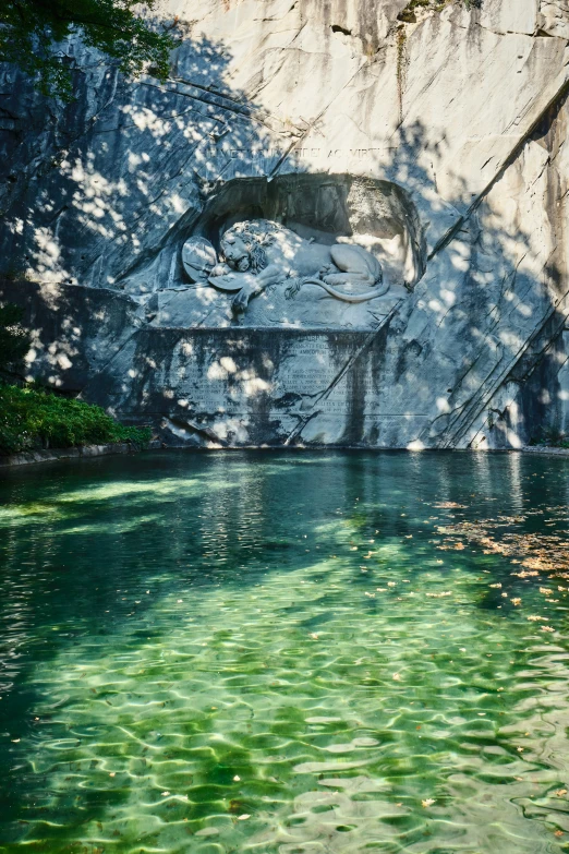 green water beneath a rock formation with a small waterfall behind it