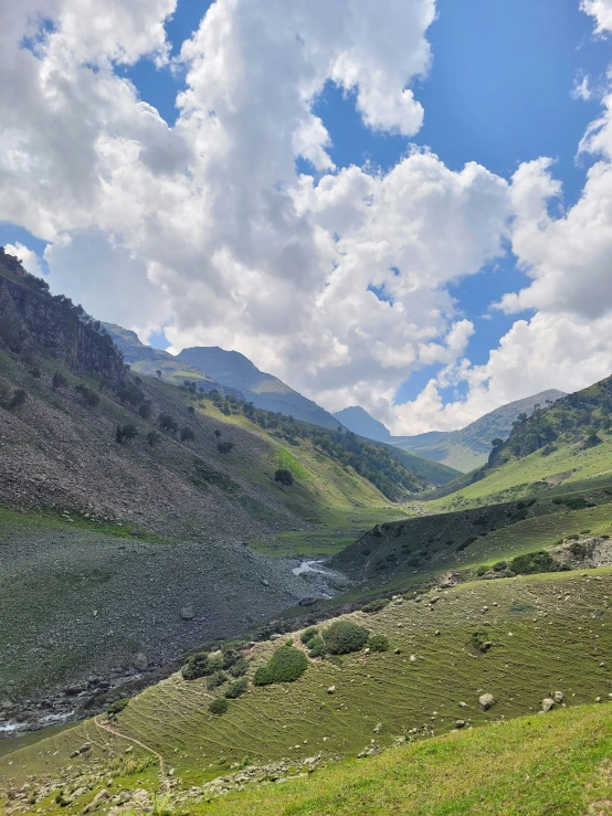 a lush green valley surrounded by mountains under a cloudy sky