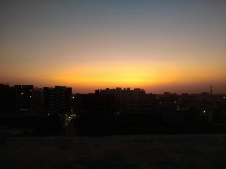 buildings are silhouetted against a dusk sky and the sun in the distance