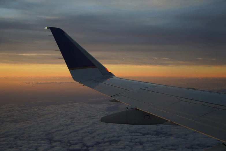 an airplane wing in the sky at dusk with the clouds below it