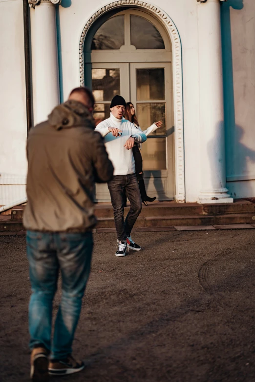 two men outside a building watching another man perform a trick