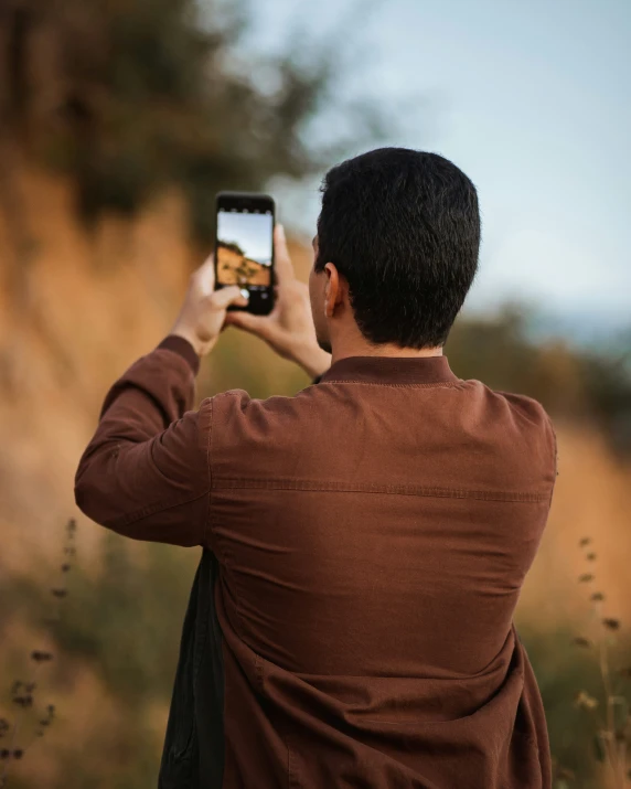 a man in brown shirt taking pictures on his cell phone