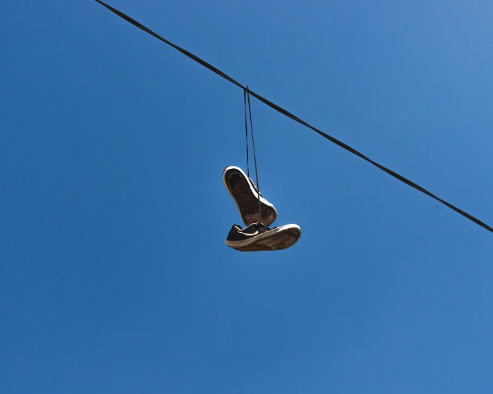 a pair of shoes hanging from a wire with a blue sky in the background