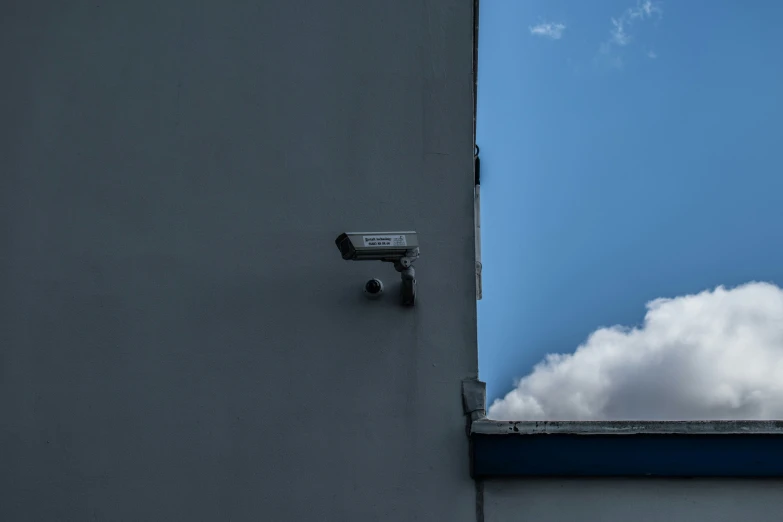 a security camera outside the window of a building with some clouds behind it