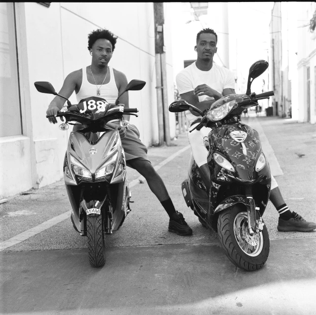a couple of men standing next to their motor scooters