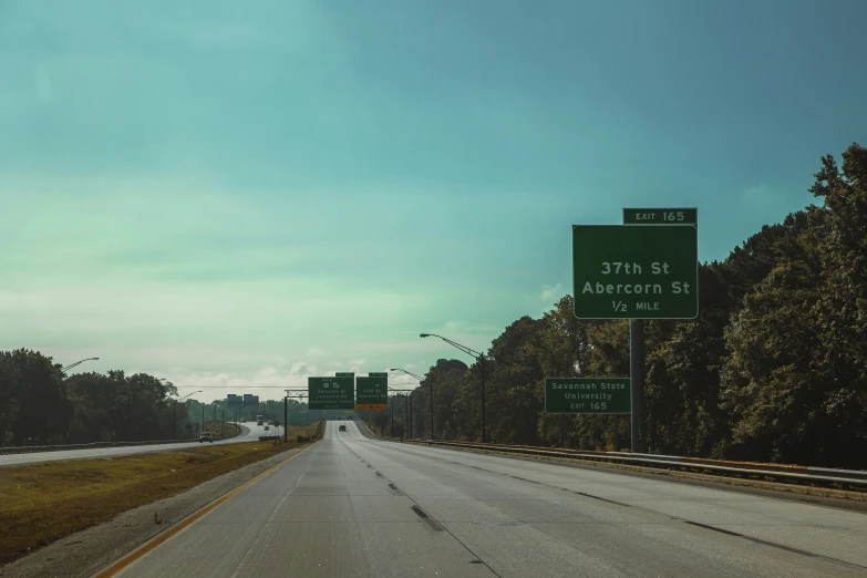 a highway with green signs and trees in the background