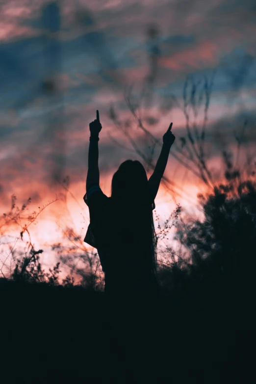 a silhouetted girl in the dark holds up her hands to the sky