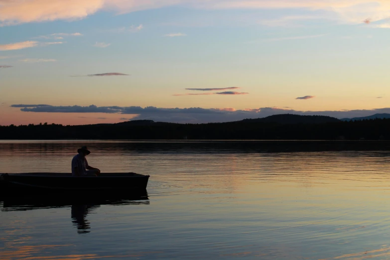 a man sitting in a rowboat on a lake at sunset