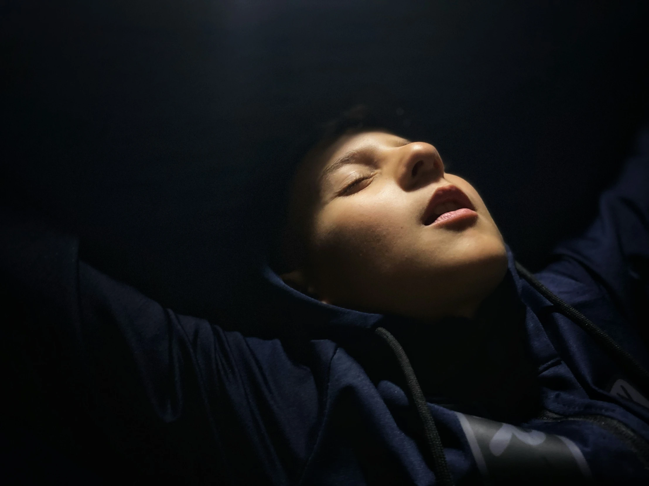 a young man laying in the dark with his head held up to him by two hands