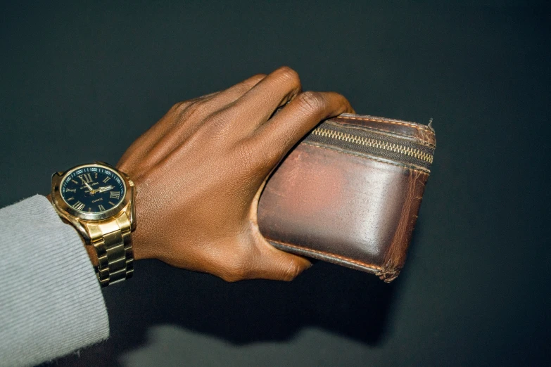 a mans hand and wrist holding a watch with leather wallet
