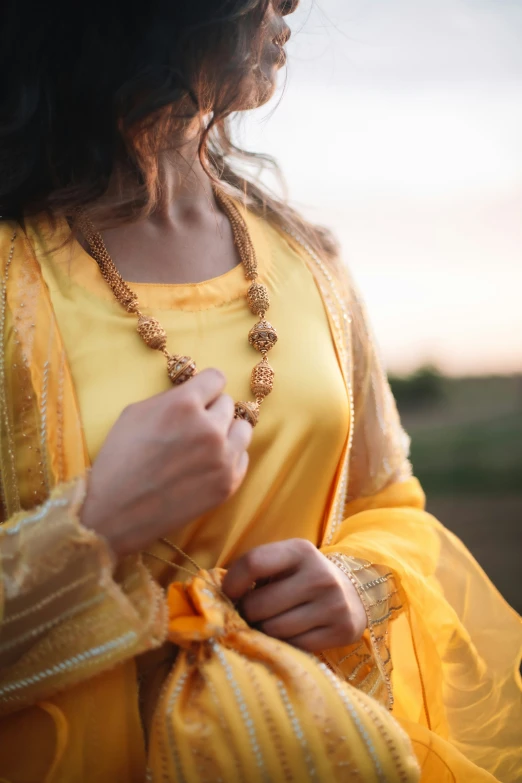 an indian woman is wearing gold jewelry and holding a yellow shawl