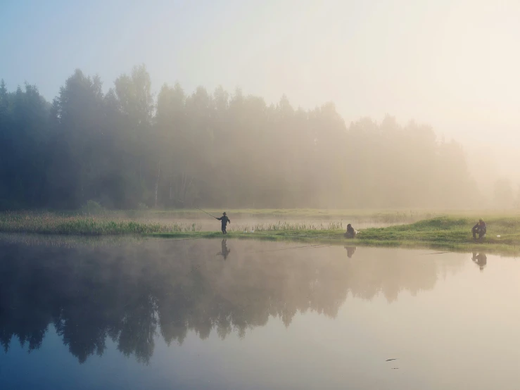 some people are walking along the water in the fog