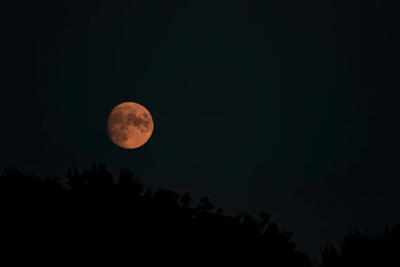 the moon is glowing orange in the night sky