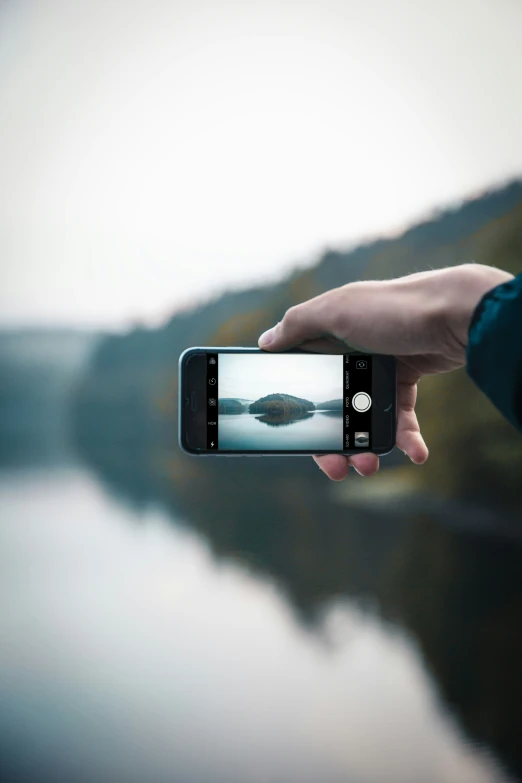 a person holding up a phone taking a po of a body of water