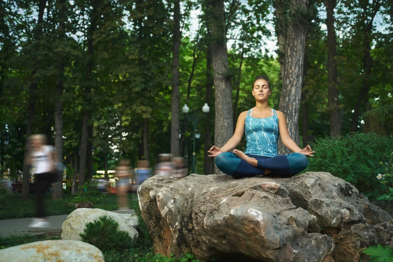 woman sitting on rock doing yoga in a park