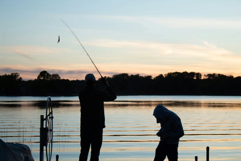 two men on a pier fish off of a boat