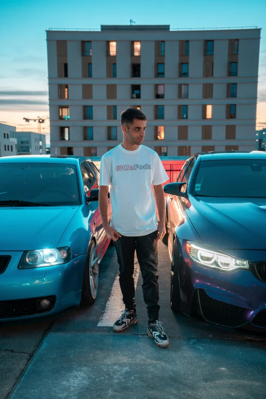 a young man stands next to three cars