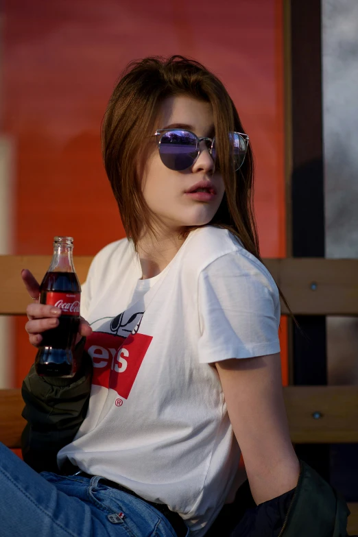 woman in sunglasses sitting on bench holding coke in her hand