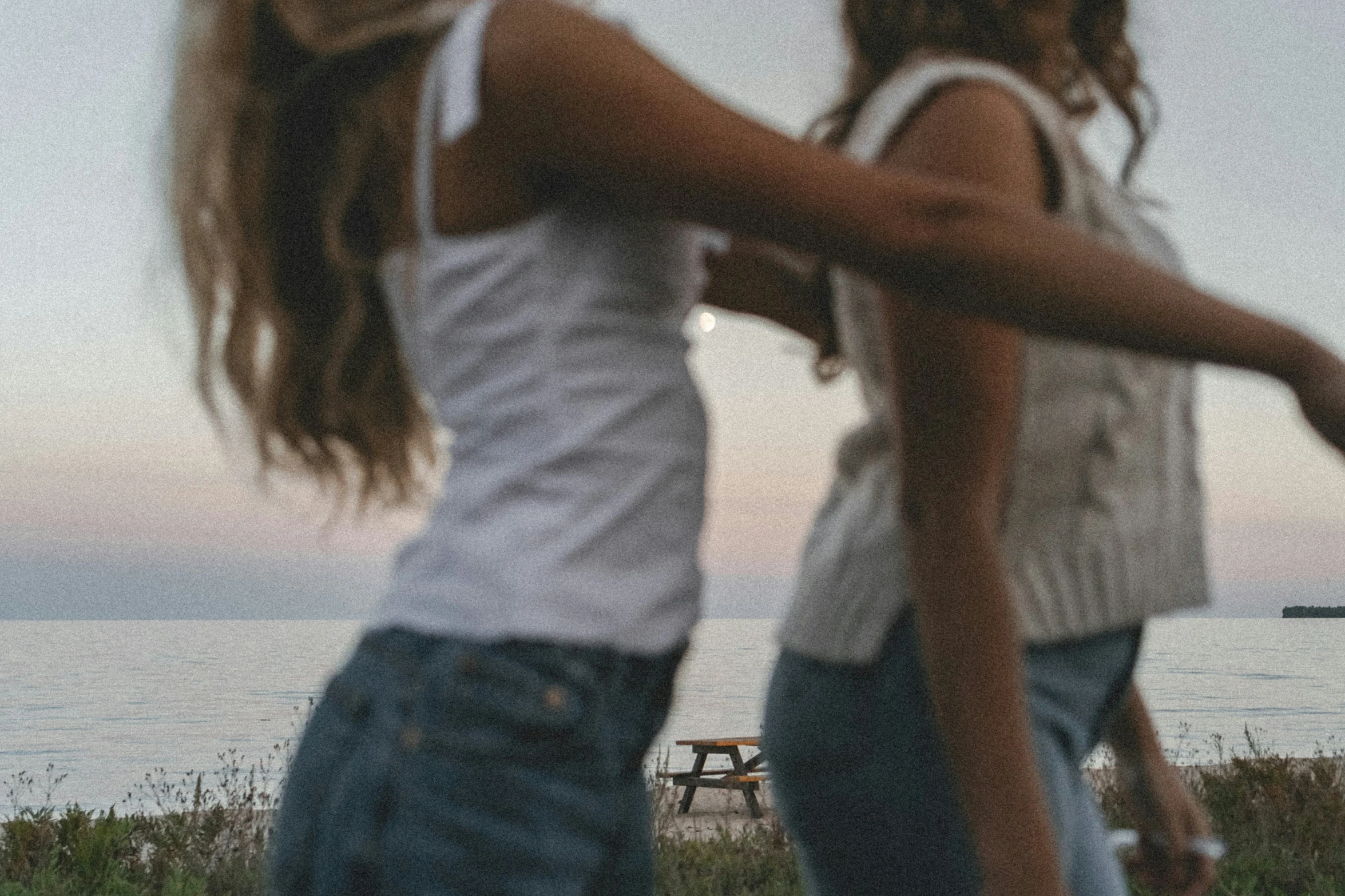 two girls playing frisbee near the ocean on a cloudy day