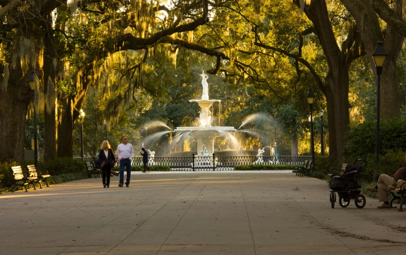 people are walking and sitting in the park by a fountain