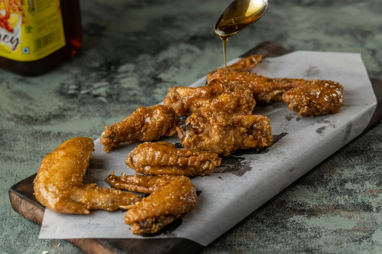 a person pouring teriyaki sauce over chicken wings on a tray