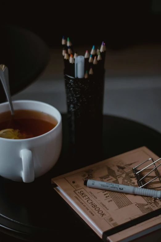 cup of tea, books and pens are sitting on a table