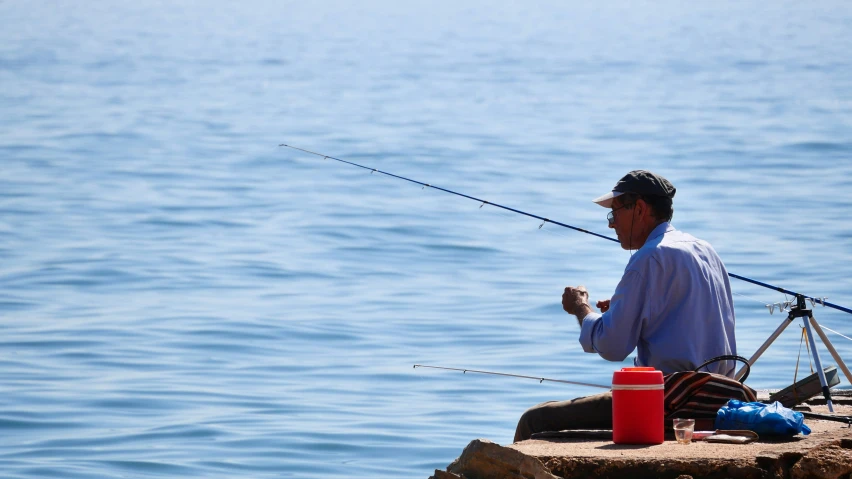 the man sits on the rocks with his fishing rod