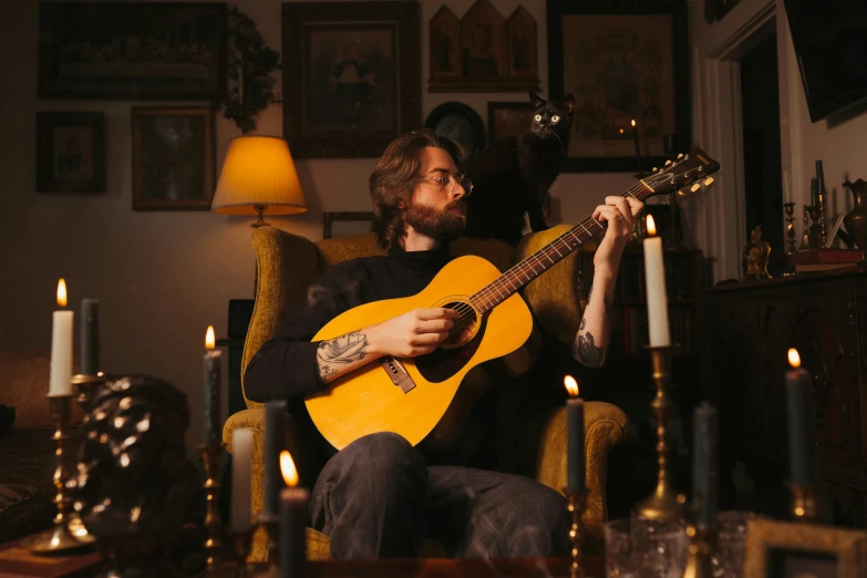 man with beard sitting on yellow chair and playing guitar