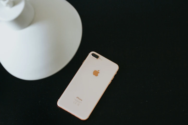 an iphone laying next to a white vase on top of a table