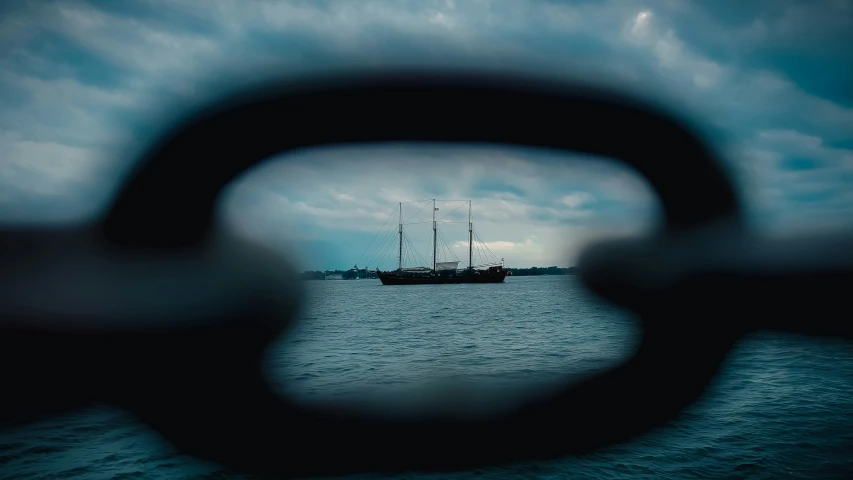 an image looking through a fence at the ocean and a ship