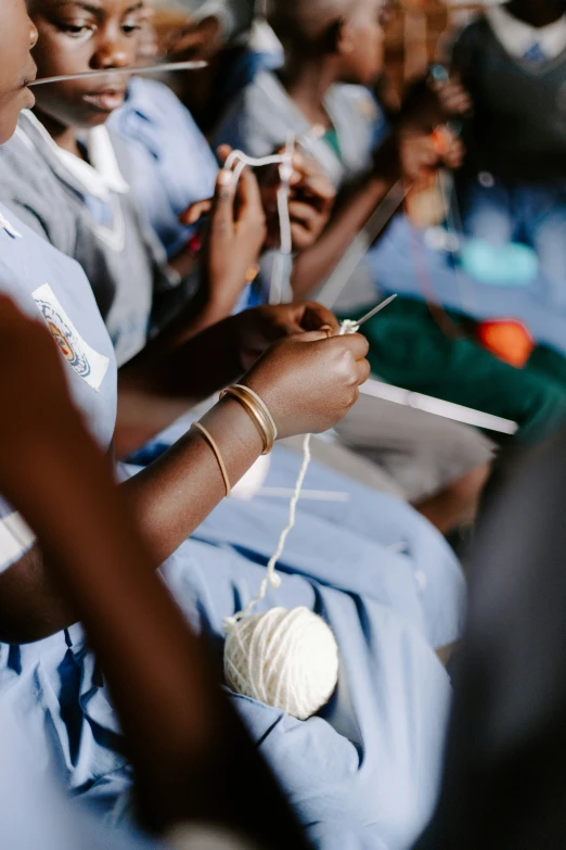 a group of girls sitting in a room holding some type of knitting needle