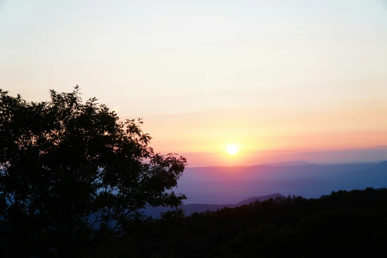 a sunset over trees in front of the mountains