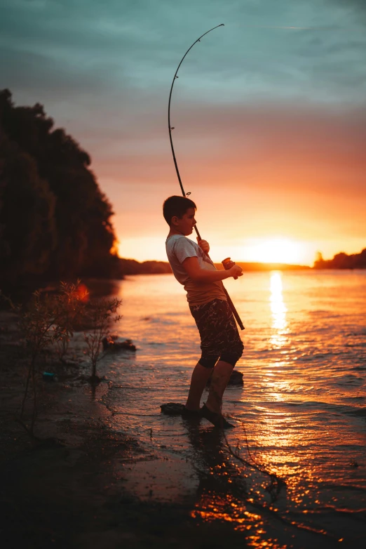 the young child is fishing at sunset on the lake