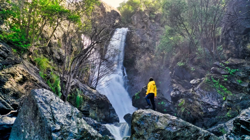 the man is standing on top of a rock above a waterfall