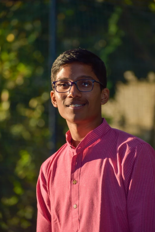 a man wearing glasses standing next to a fence