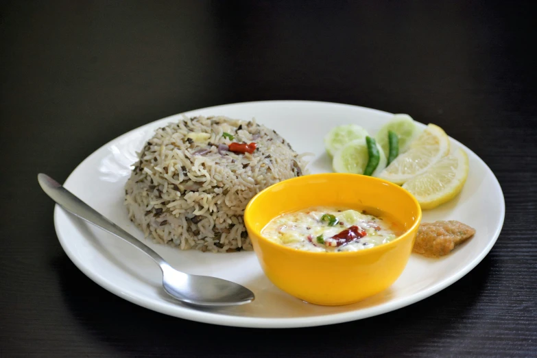 plate of food on table with a silver spoon, cup, rice ball, and fruit