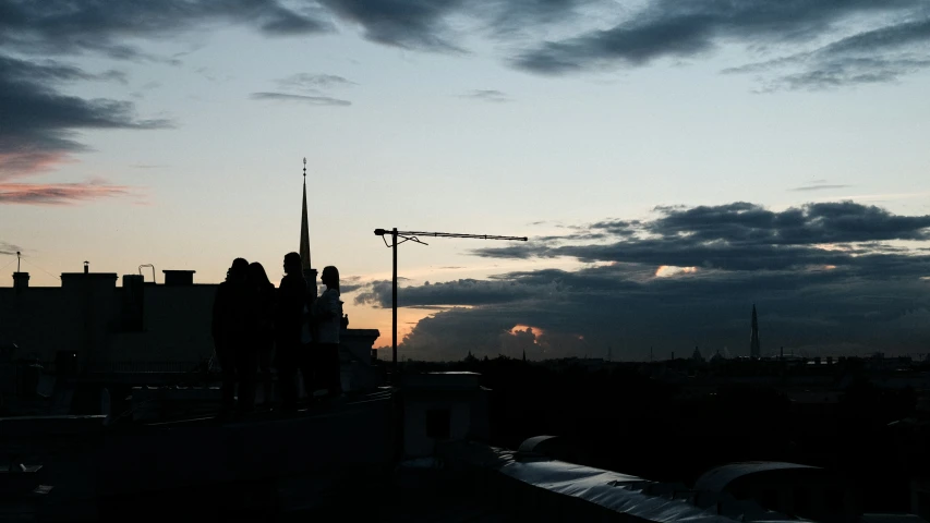 several people in silhouette on a roof with the sun setting
