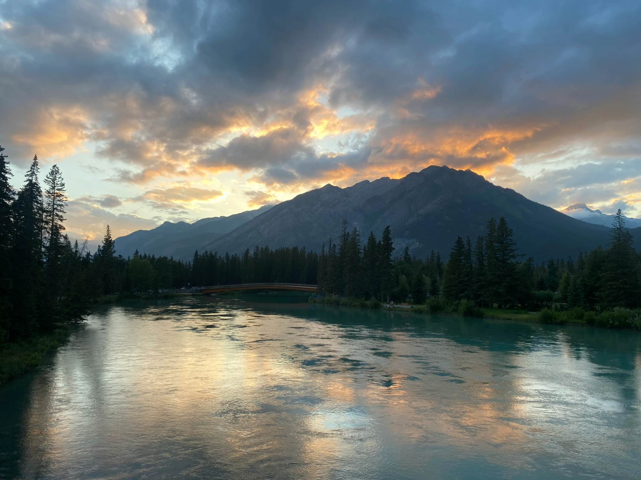 a river runs between pine trees under a mountain