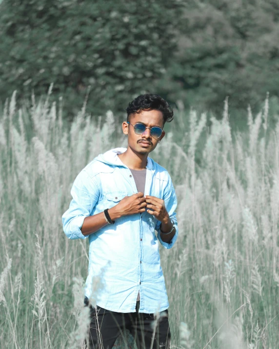 a young man with sunglasses standing in a grassy field